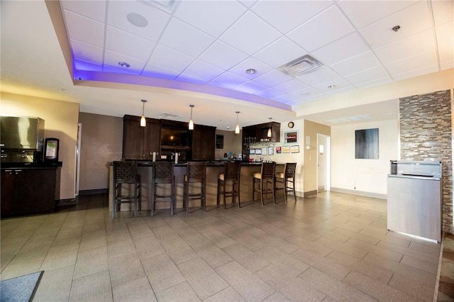 kitchen with baseboards, a breakfast bar, a tray ceiling, a drop ceiling, and dark brown cabinetry