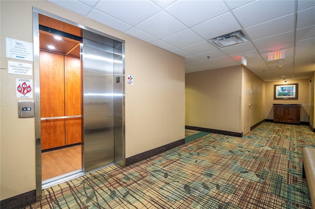 hall with a drop ceiling, visible vents, baseboards, and elevator