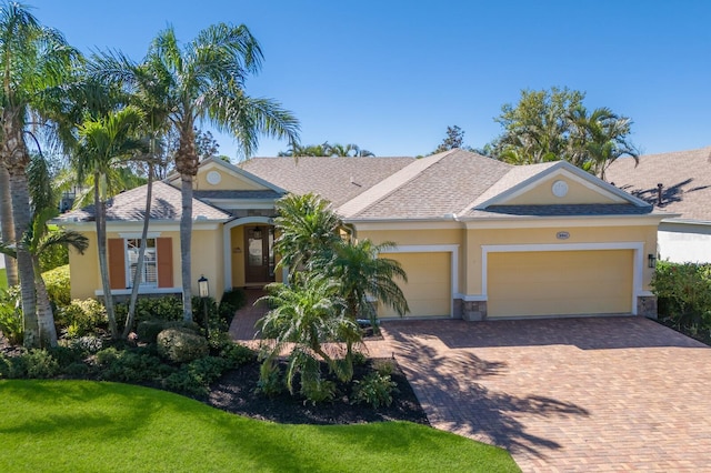 view of front of home featuring stucco siding, decorative driveway, a garage, and a front lawn