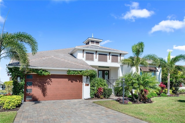 view of front of house with an attached garage, stucco siding, a front lawn, a tiled roof, and decorative driveway