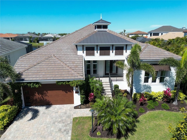 view of front of house with covered porch, stucco siding, metal roof, decorative driveway, and a garage