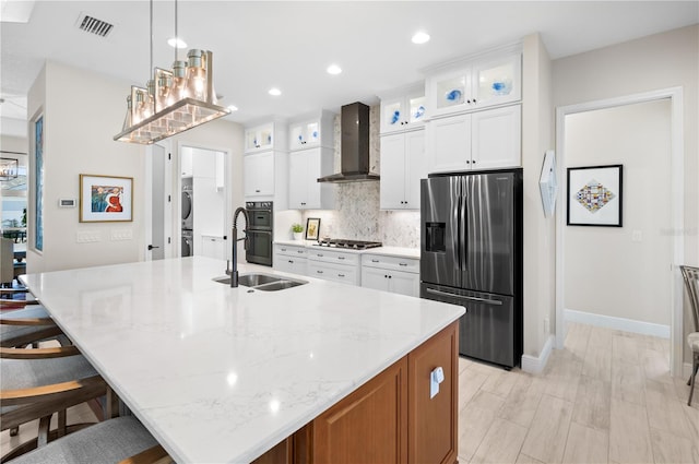 kitchen featuring visible vents, a sink, stainless steel appliances, wall chimney exhaust hood, and decorative backsplash