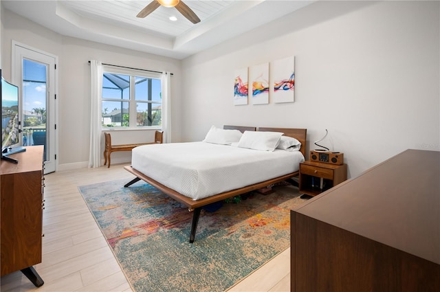 bedroom with light wood-style flooring, a tray ceiling, recessed lighting, baseboards, and ceiling fan