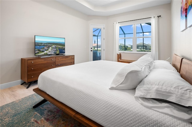 bedroom featuring light wood-type flooring, baseboards, a raised ceiling, and access to outside