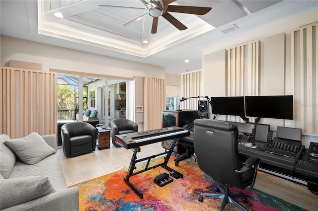 home office with ceiling fan, a tray ceiling, visible vents, and wood finished floors