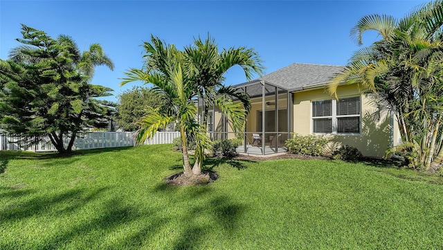 view of yard featuring glass enclosure, ceiling fan, and fence