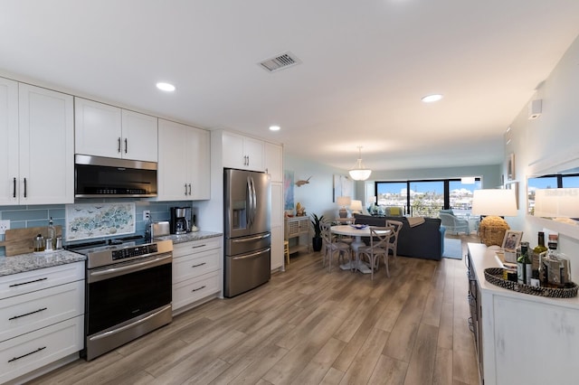 kitchen with visible vents, light wood-style flooring, appliances with stainless steel finishes, tasteful backsplash, and open floor plan