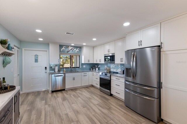 kitchen with visible vents, decorative backsplash, white cabinets, stainless steel appliances, and a sink