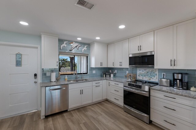 kitchen with visible vents, backsplash, stainless steel appliances, white cabinetry, and a sink