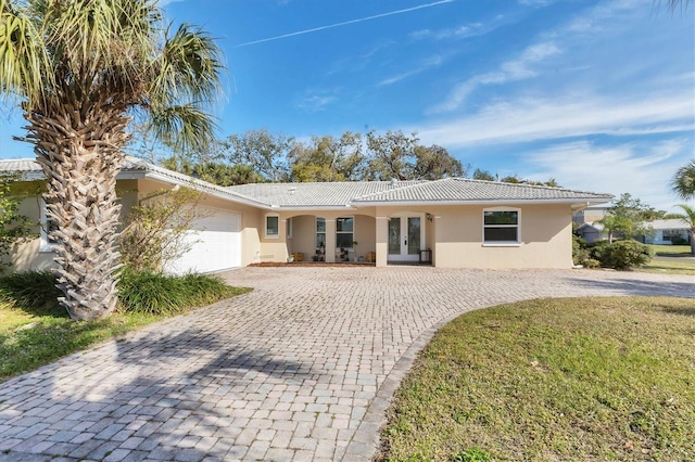 ranch-style house with stucco siding, a tile roof, decorative driveway, french doors, and an attached garage