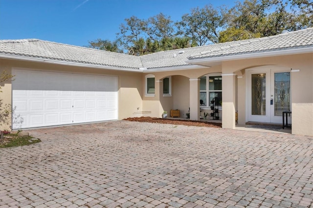 rear view of house featuring an attached garage, stucco siding, french doors, a tiled roof, and decorative driveway