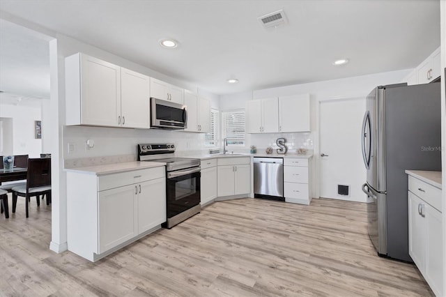 kitchen with visible vents, a sink, stainless steel appliances, white cabinets, and light countertops