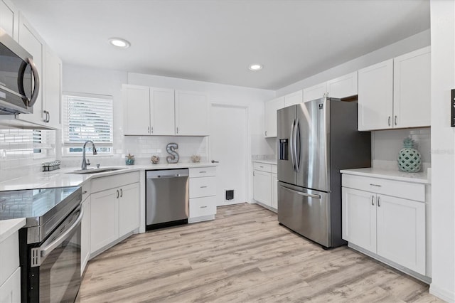 kitchen featuring light wood-type flooring, a sink, tasteful backsplash, appliances with stainless steel finishes, and white cabinets