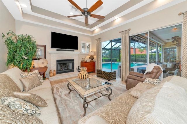 living area featuring visible vents, a fireplace with raised hearth, ceiling fan, a sunroom, and a raised ceiling