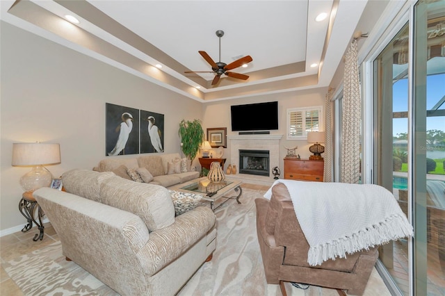 living area featuring baseboards, a tiled fireplace, recessed lighting, a raised ceiling, and a ceiling fan