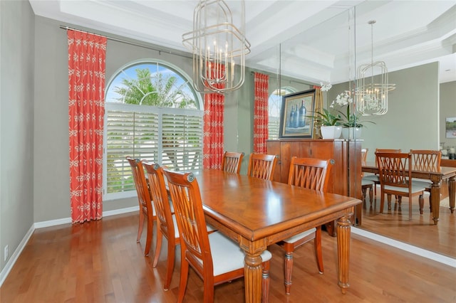 dining area with a raised ceiling, a notable chandelier, a healthy amount of sunlight, and wood finished floors