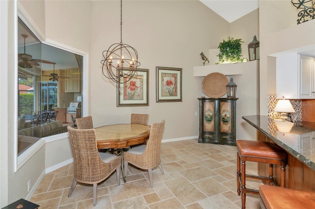 dining room featuring ceiling fan with notable chandelier, stone finish floor, baseboards, and a towering ceiling