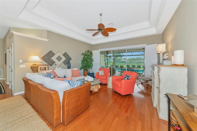 living area featuring a tray ceiling, a ceiling fan, light wood-type flooring, and baseboards