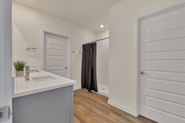full bathroom with wood finished floors, tiled shower, double vanity, recessed lighting, and a sink