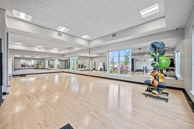 exercise room featuring visible vents, a raised ceiling, baseboards, and wood finished floors