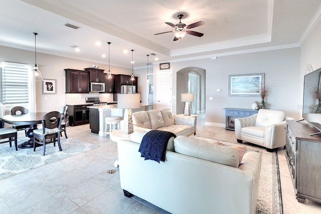 living area featuring arched walkways, visible vents, crown molding, and a tray ceiling