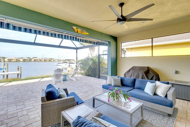 view of patio with glass enclosure, ceiling fan, a water view, and an outdoor hangout area