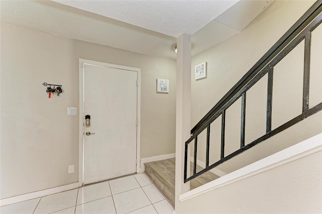 foyer with light tile patterned flooring, stairway, a textured ceiling, and baseboards