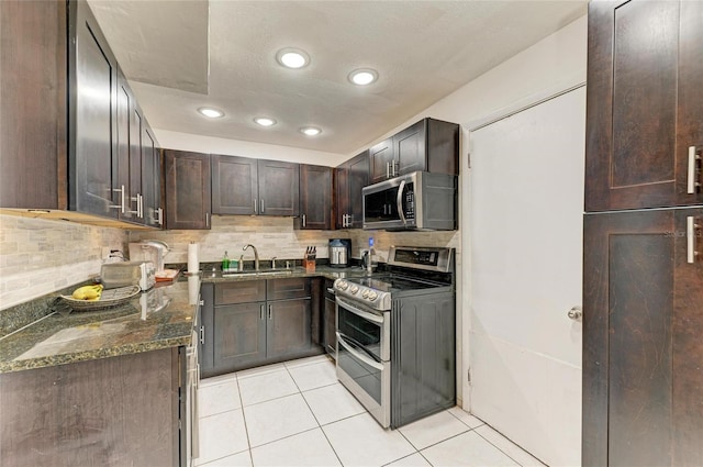 kitchen featuring dark stone countertops, light tile patterned flooring, a sink, appliances with stainless steel finishes, and backsplash