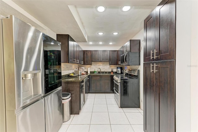 kitchen featuring dark stone counters, decorative backsplash, appliances with stainless steel finishes, light tile patterned flooring, and a sink