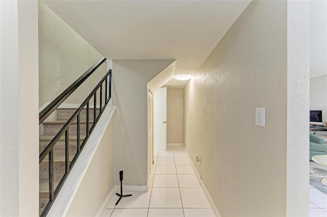 hallway featuring a textured ceiling, tile patterned flooring, baseboards, stairs, and a textured wall