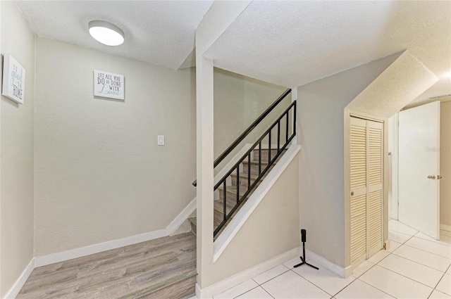 staircase with wood finished floors, baseboards, and a textured ceiling