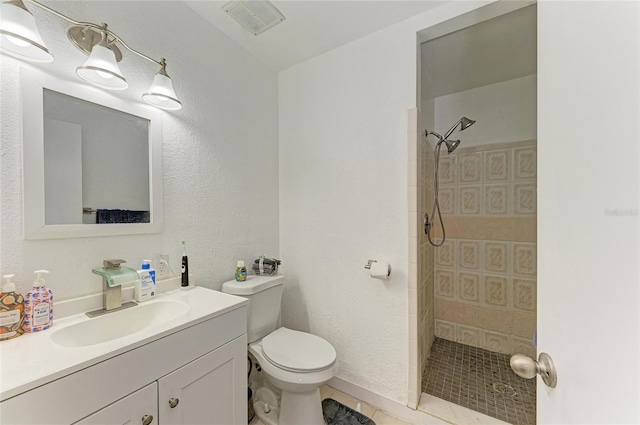 bathroom with vanity, visible vents, tiled shower, toilet, and a textured wall