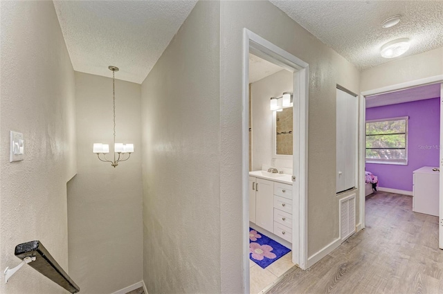 corridor featuring an inviting chandelier, a sink, light wood-style floors, a textured ceiling, and a textured wall