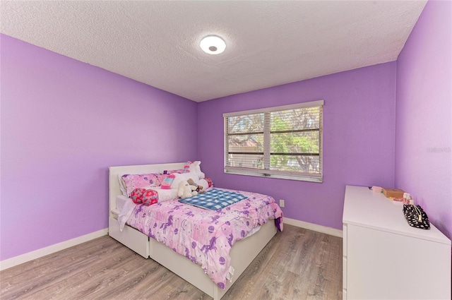 bedroom with light wood-style flooring, a textured ceiling, and baseboards