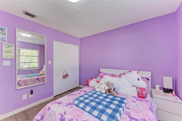 bedroom featuring visible vents, a textured ceiling, wood finished floors, a closet, and baseboards