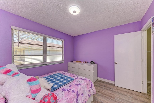 bedroom with baseboards, a textured ceiling, and wood finished floors