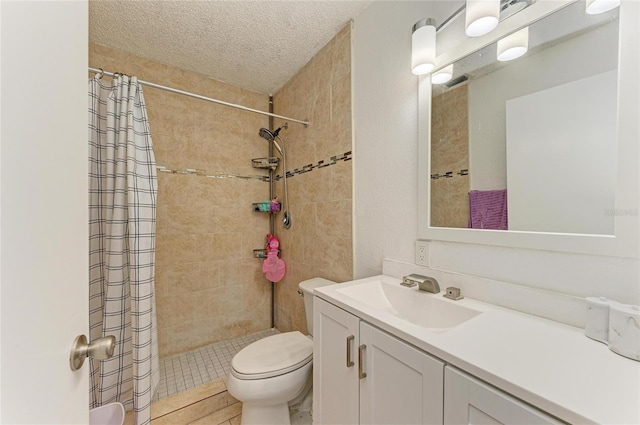 full bath featuring vanity, toilet, a tile shower, and a textured ceiling