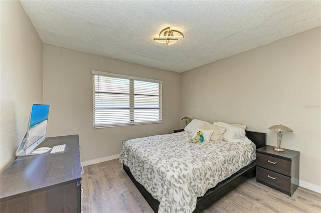 bedroom featuring baseboards, light wood-style floors, and a textured ceiling