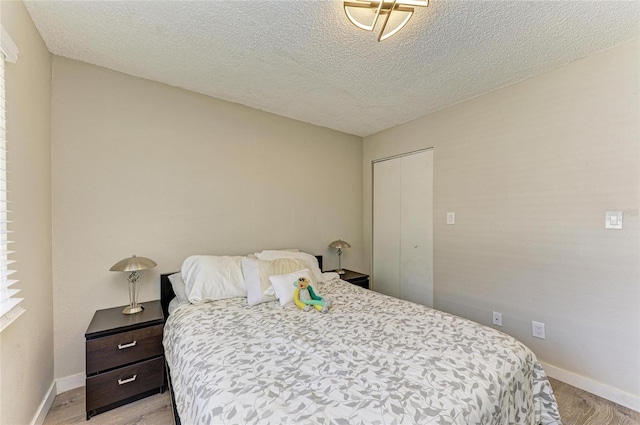 bedroom with a textured ceiling, baseboards, and light wood-style floors