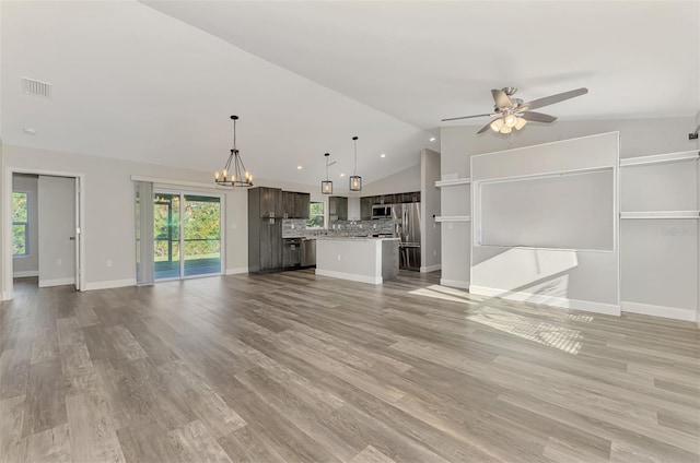 unfurnished living room featuring lofted ceiling, ceiling fan with notable chandelier, light wood-style floors, and a healthy amount of sunlight