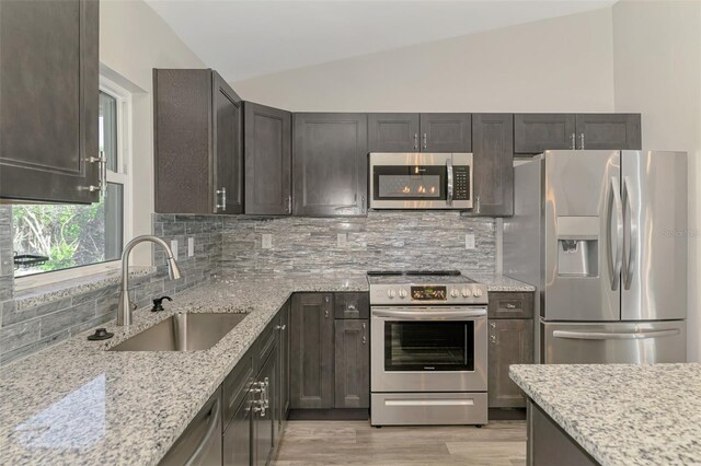 kitchen featuring a sink, vaulted ceiling, decorative backsplash, and stainless steel appliances