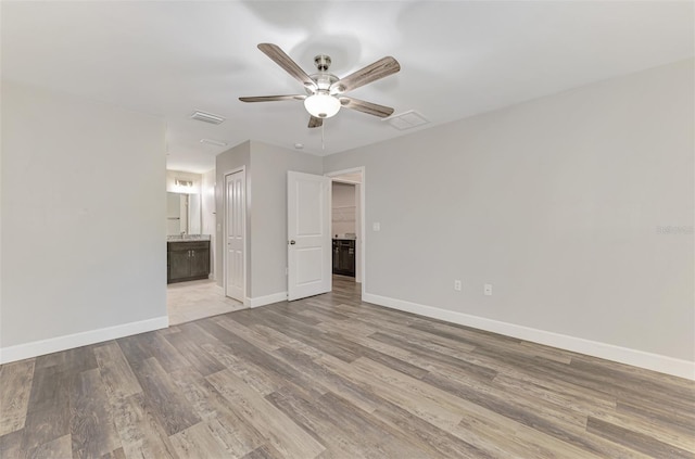 unfurnished bedroom with wood finished floors, visible vents, baseboards, ensuite bath, and a closet