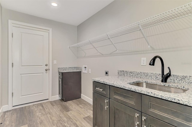 laundry room with baseboards, hookup for a washing machine, light wood-style floors, hookup for an electric dryer, and a sink