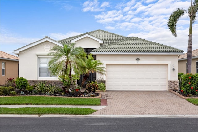 ranch-style house featuring an attached garage, stucco siding, stone siding, a tiled roof, and decorative driveway