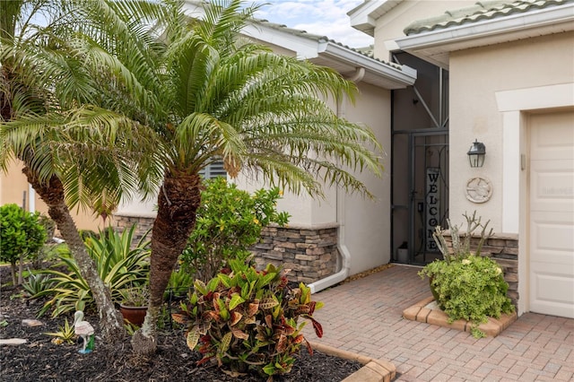 entrance to property with stucco siding, stone siding, and a garage