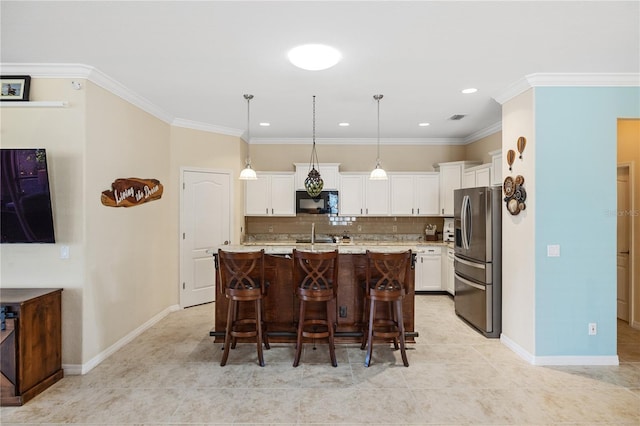 kitchen featuring decorative backsplash, black microwave, white cabinetry, stainless steel fridge, and a kitchen bar