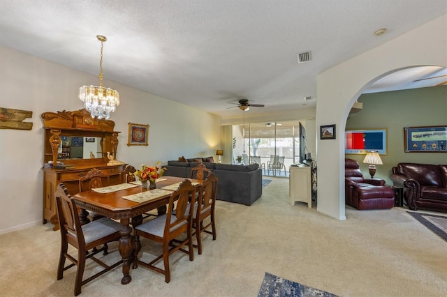 dining area featuring visible vents, arched walkways, a textured ceiling, ceiling fan with notable chandelier, and light colored carpet