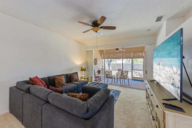 living area featuring a textured ceiling, a ceiling fan, visible vents, and light carpet