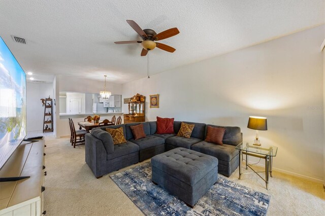 living area featuring baseboards, ceiling fan with notable chandelier, light colored carpet, and a textured ceiling