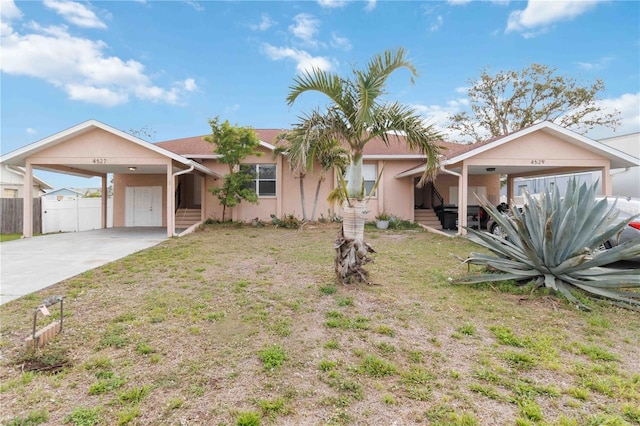 ranch-style house with an attached carport, fence, stucco siding, concrete driveway, and a front lawn